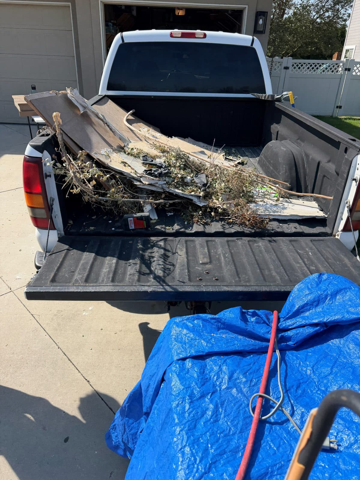 Pickup truck with the tailgate down, bed loaded with branches, brush, and torn-out board from a Treasure Valley yard clearing